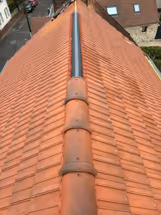Faîtage en cours de pose sur une couverture en tuiles neuves, faîtières rondes sur la moitié avant, rouleau de closoir encore apparent derrière